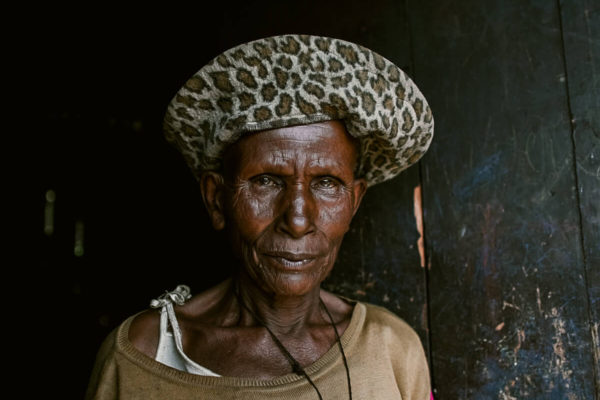 Older woman wearing leopard print hat and crucifix starting directly at the camera